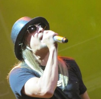 Kid Rock singing into a microphone wearing a hat and sunglasses
