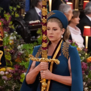 Penny Mordaunt looking ridiculous in some sort of blue outfit and shoulder cape with gold detail holding a sword at the coronation