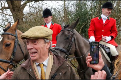 Nigel Farage looking like a cartoon rural-type with a wax jacket and flat cap. Behind him are two Fox hunters on horses wearing scarlet jackets and black helmets