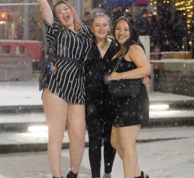 Three young women in thin short dresses or leggings standing in the snow looking happy on a night out clubbing