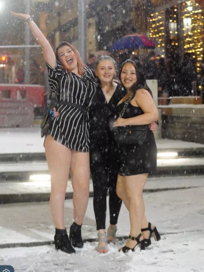 Three young women in thin short dresses or leggings standing in the snow looking happy on a night out clubbing