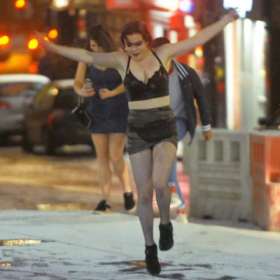 A young women in black shorts and a black bra top dancing in the snow looking happy on a night out clubbing