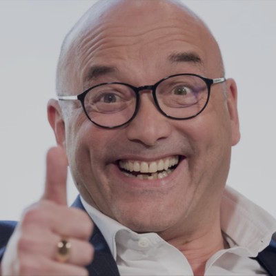 Greg Wallace, mature bald man wearing dark frame glasses. He is grinning broadly and is doing a thumbs up to the camera