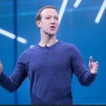 Mark Zuckerberg at a presentation in a blue top against a blue background with random white stripes