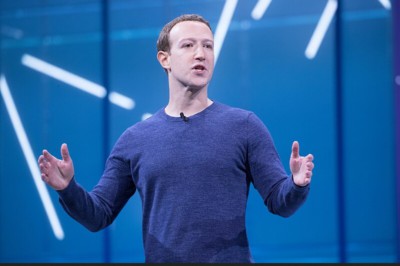 Mark Zuckerberg at a presentation in a blue top against a blue background with random white stripes