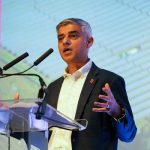 Sadiq Khan at a podium giving a speech. A mature Asian man with short grey hair in a dark jacket and a white shirt.