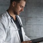 Male doctor in a white coat with a stethoscope around his neck looking at notes