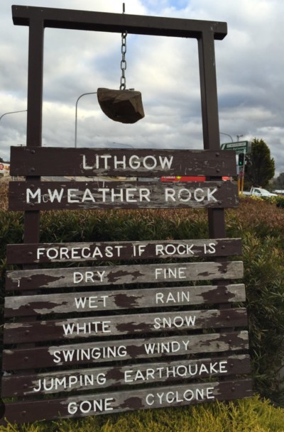 A rock hanging on a frame with panels saying: forecast if rock is: dry - fine, wet - rain, white - snow, swinging - windy, jumping - earthquake, gone - cyclone.