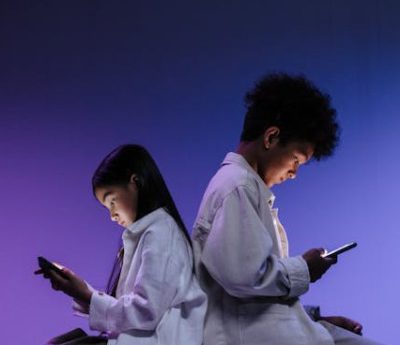 Kids Sitting Back to back Using Smartphones. Plain purple background fading to black at the top