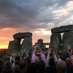 Lots of people holding up phones as sun rises at Stonehenge during summer solstice sunrise