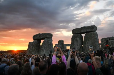 Lots of people holding up phones as sun rises at Stonehenge during summer solstice sunrise