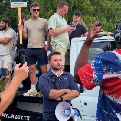 Neo-nazi agitator Callum Barker standing by a lorry with a megaphone. One of the men on the lorry is holding up a sign for Homeland - a neo-nazi group.