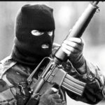 terrorist wearing a camouflage jacket and black balaclava holding a tifle