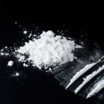 A small pile of white powder (cocaine) next to three lines of white powder on a black surface.