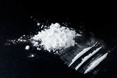 A small pile of white powder (cocaine) next to three lines of white powder on a black surface.
