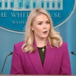 Karoline Leavitt White House press secretary. Young blonde woman with long hair. Standing at a podium talking. The US flag to the to the right and the white house emblem behind her.