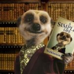 Meerkat character from compare the market.com adverts. A furry meerkat wearing a smoking jacket and cravat holding up in a book with books on shelves in the background.