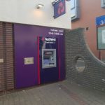 A cash point machine with a section of wall next to it with a round hole in it.
