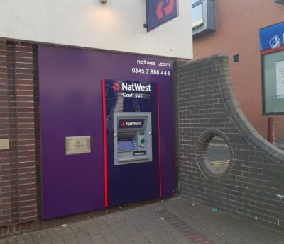 A cash point machine with a section of wall next to it with a round hole in it.