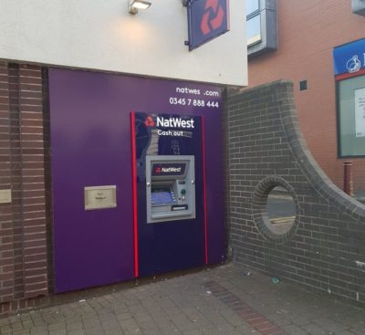 A cash point machine with a section of wall next to it with a round hole in it.